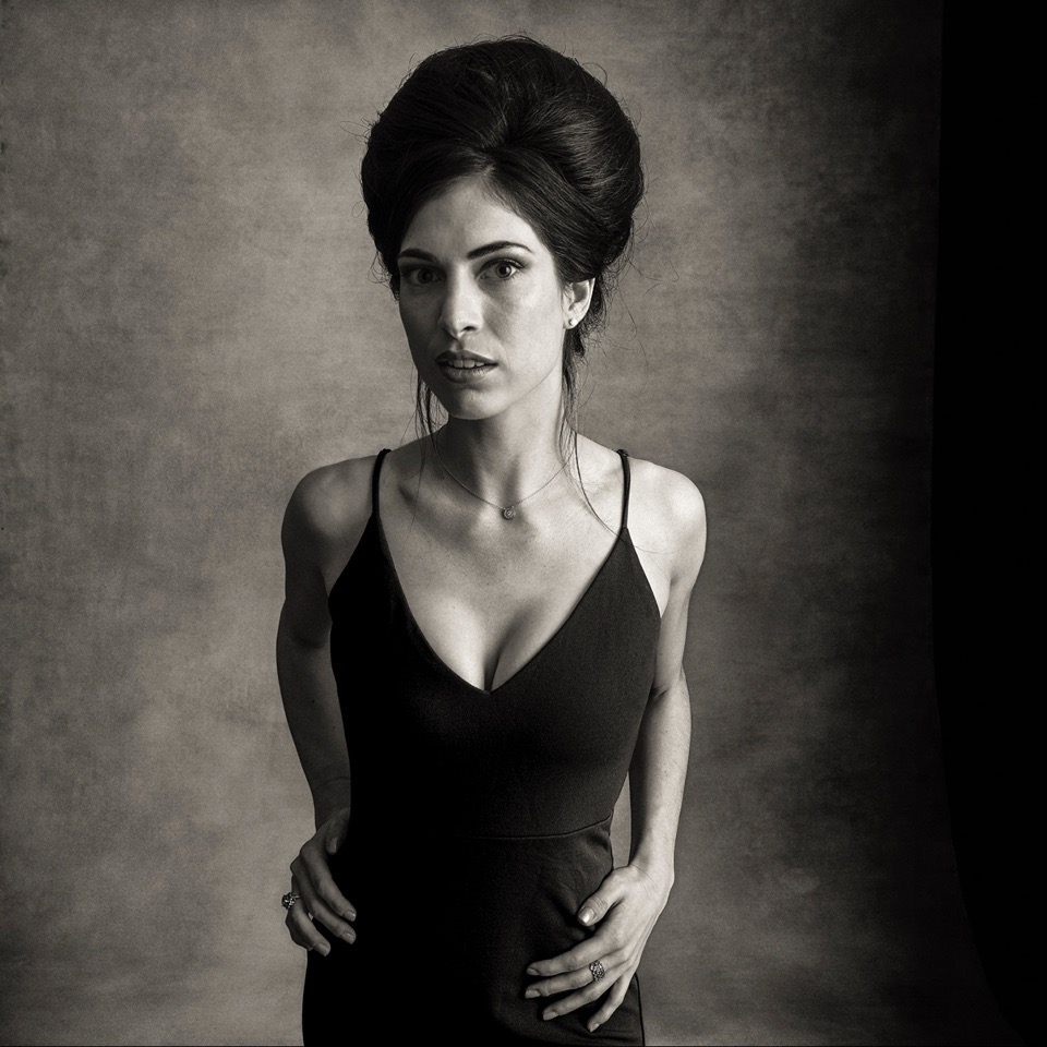 A woman stands with beehive hair in a black cocktail dress.