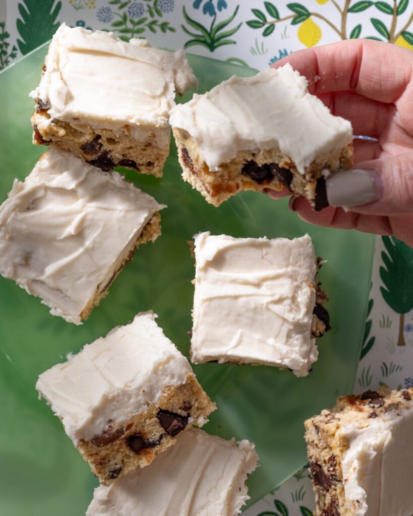 A person holds up a Bourbon Cookie Bar with a btie out of it amongst a table of other cookie bars.
