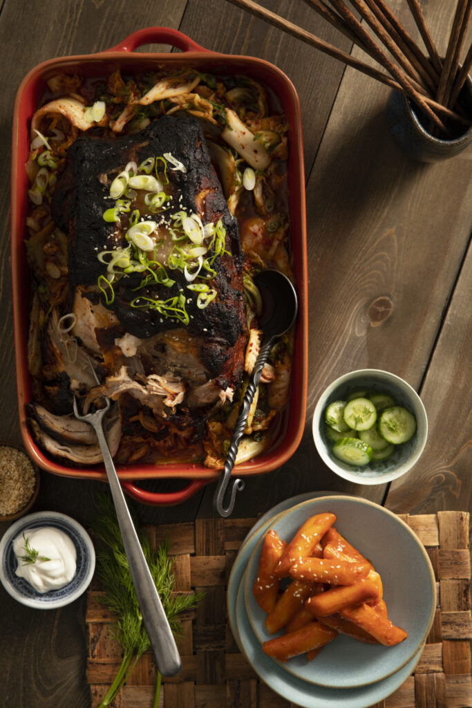 A tantalizinbraised pork shoulder & kimchi soup featuring Korean flavors, garnished with fresh dill, sour cream, scallions, and toasted sesame seeds.