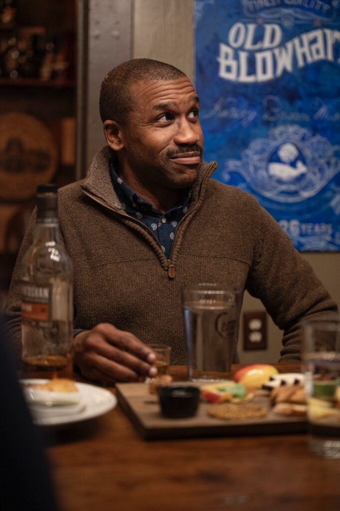 A man in a dark brown shirt listens at a scotch tasting table.