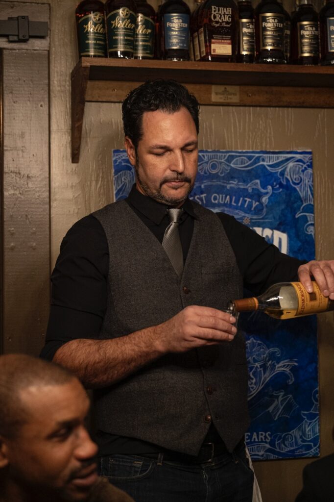 The tasting guide pours a bottle of scotch into a tasting glass.