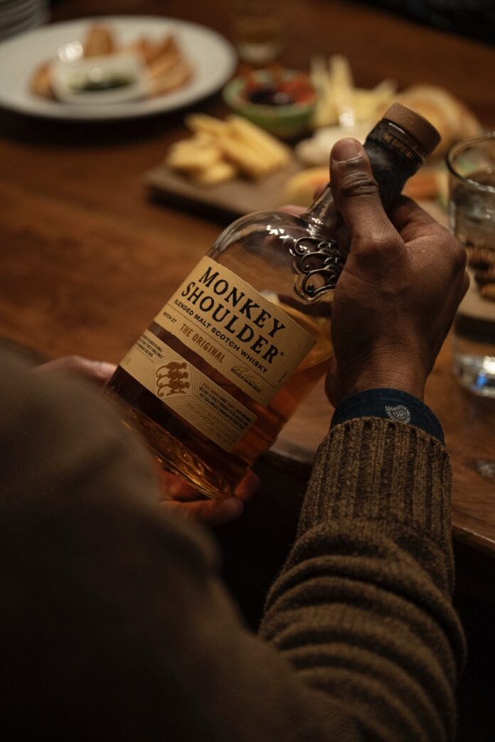 A man holds a bottle of Monkey Shoulder scotch.
