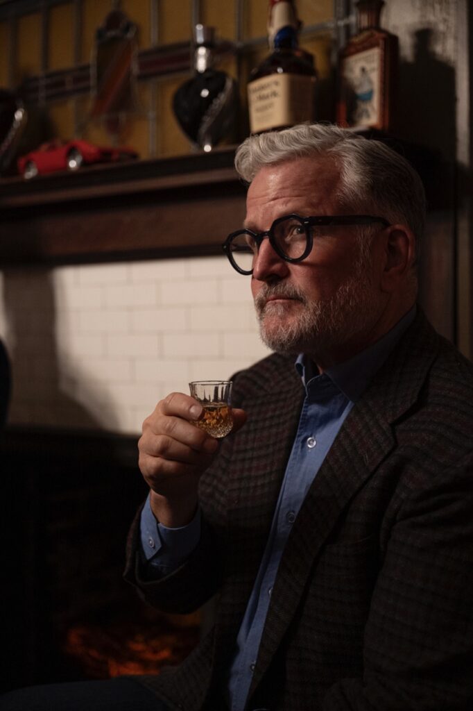 A man holds up a small glass of scotch.