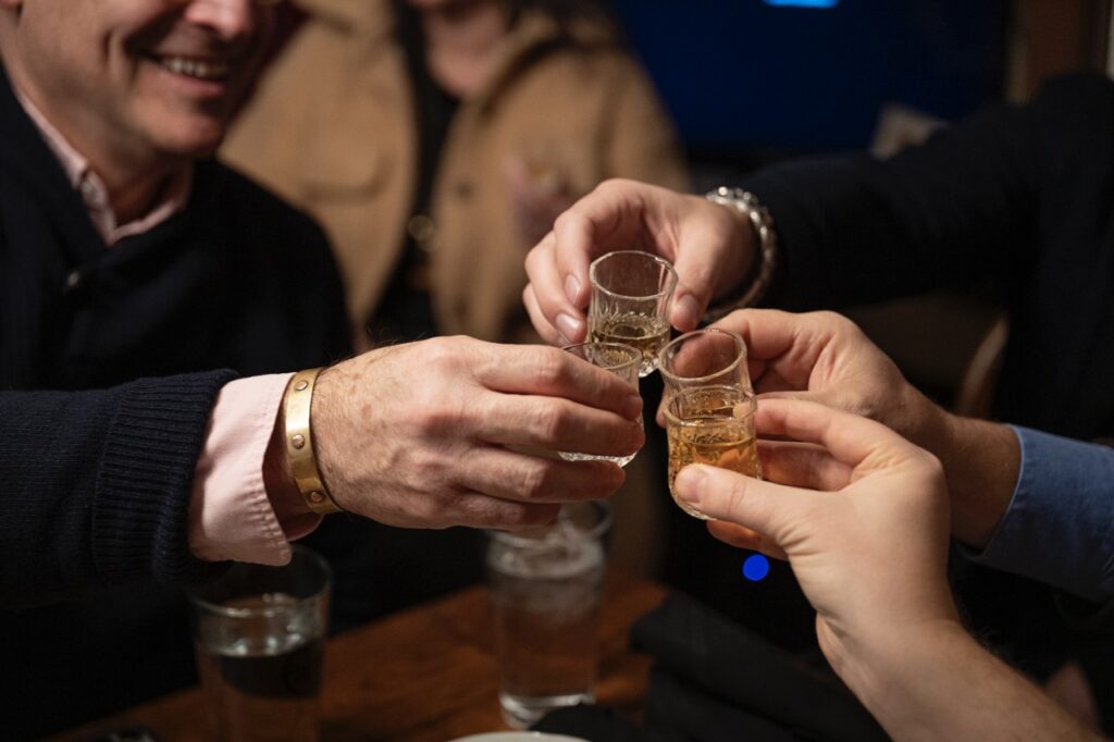 Four people cheers small glasses of scotch.