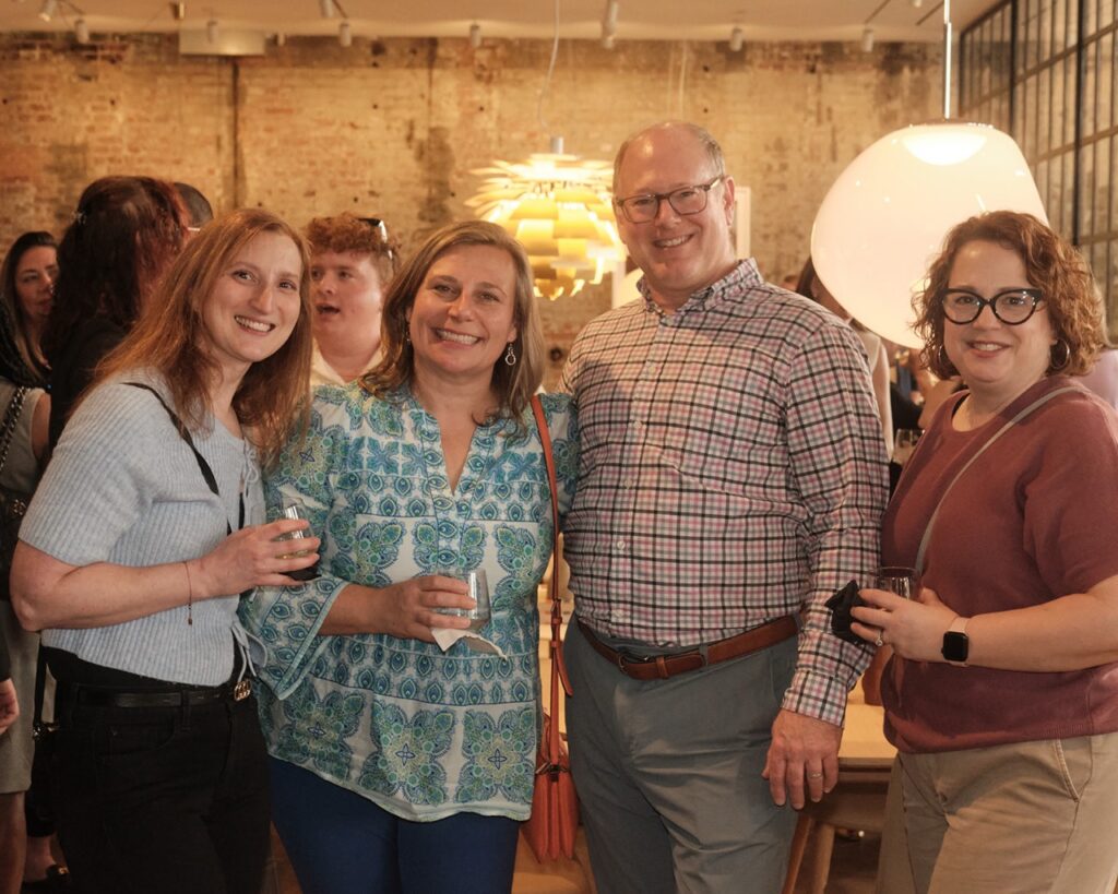 Three women in nice shirts stand with a man in a colorful plaid button up.
