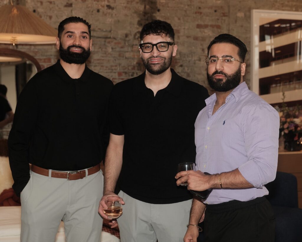 Three men in dress shirts and pants stand together.