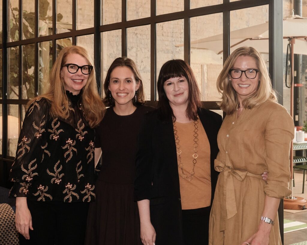 Four women smile with their arms around each other.
