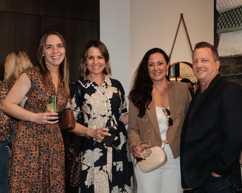 Three women stand with a man in a black suit jacket all holding drinks.