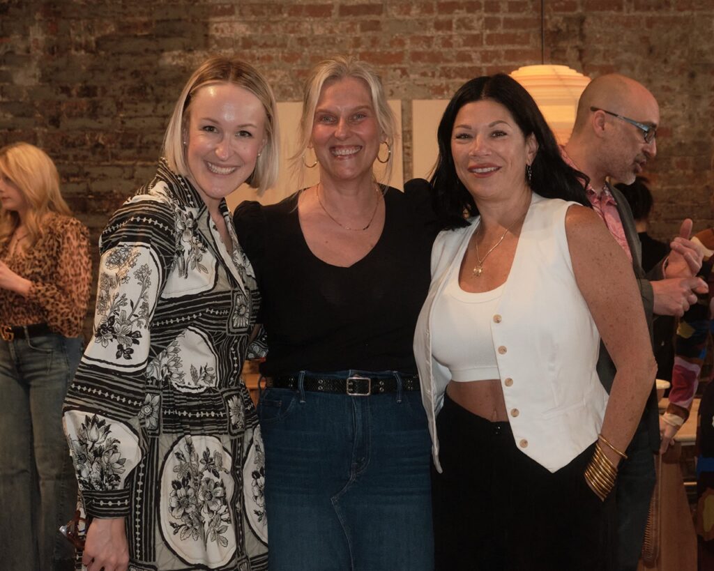 Three women smile together in white and black clothing.