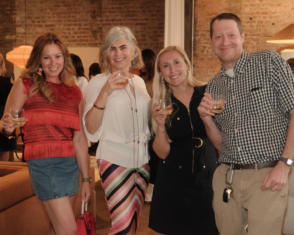 Three women and a man hold up their wine glasses while smiling.