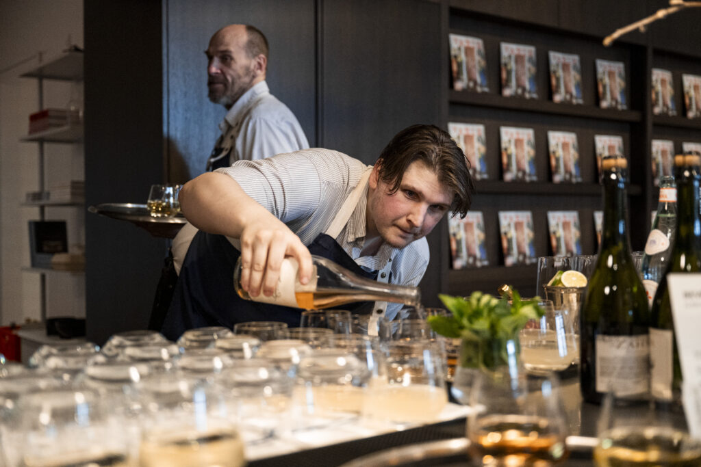 A man in an apron pours glasses of wine from a bottle.