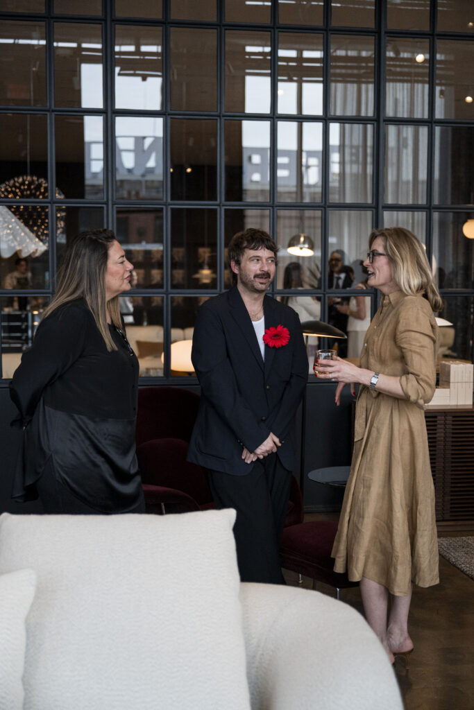 Two woman talk to a man in a black jacket with a red flower on it.