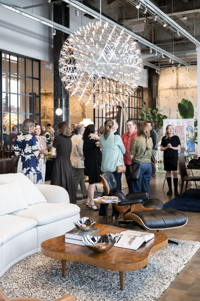People talk below a hanging ball of lights in a living room showroom.
