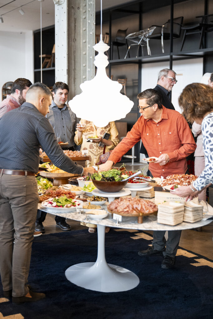 People gather around a round table full of Charcuterie, filling their plates.