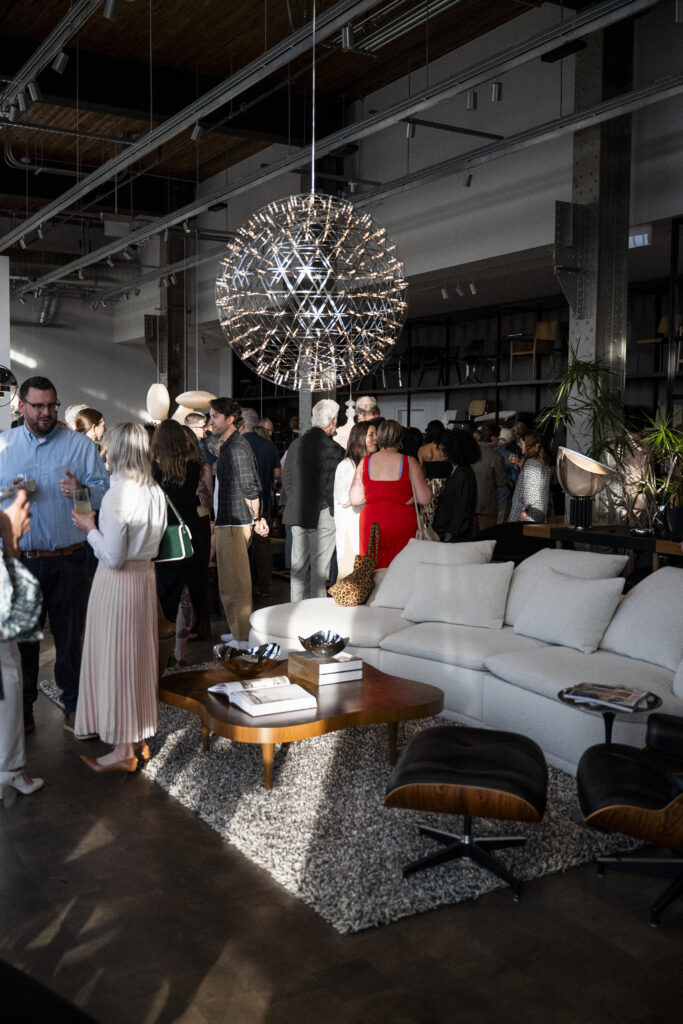 People stand in a showroom with a ball of lights, white couch, and wood coffee table.