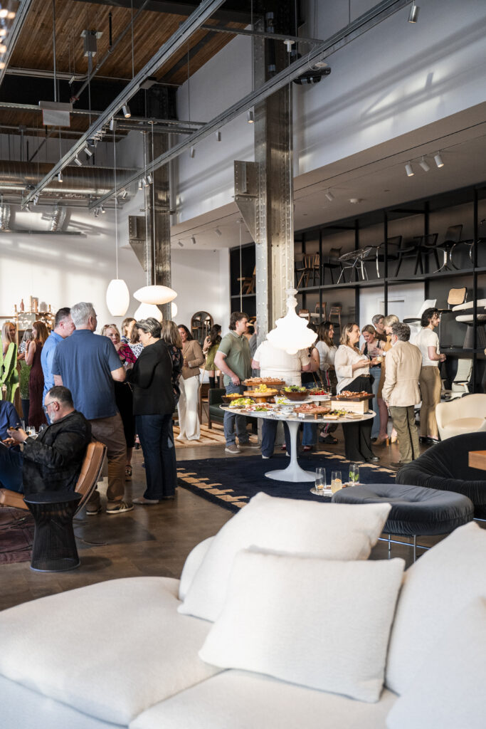 People gather in groups around the DWR showroom with a table of food in the middle.