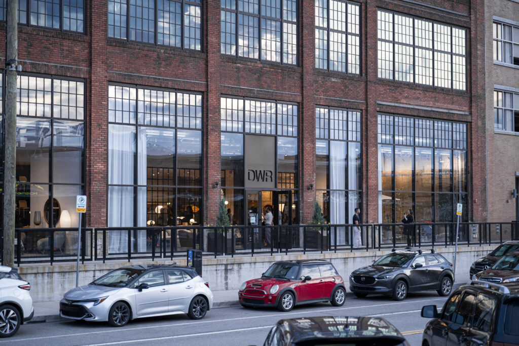 The outside of the DWR Design Within Reach building with plenty of windows and cars parked in front of it.