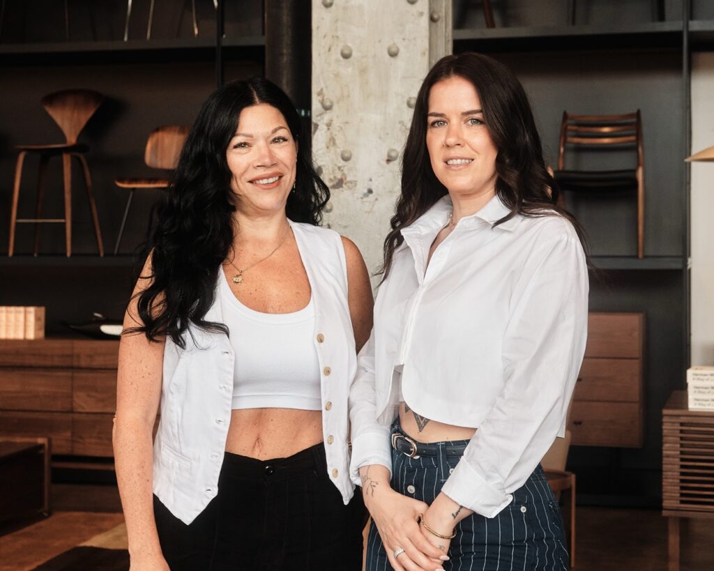 A woman in a white vest stands with a woman in a white button up crop shirt.
