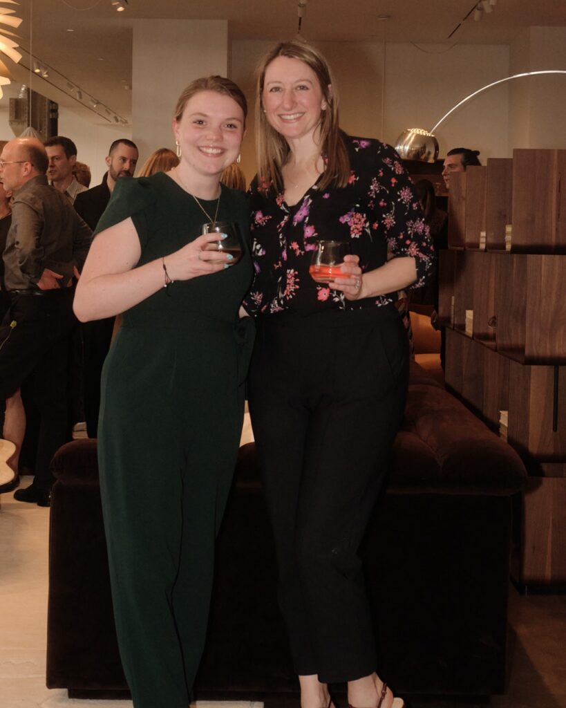 A woman in a green jumpsuit smiles with a woman in a black and pink floral top.