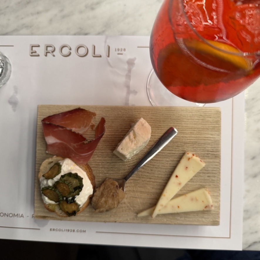 A cutting board of cheese and meats beside an aperol spritz.