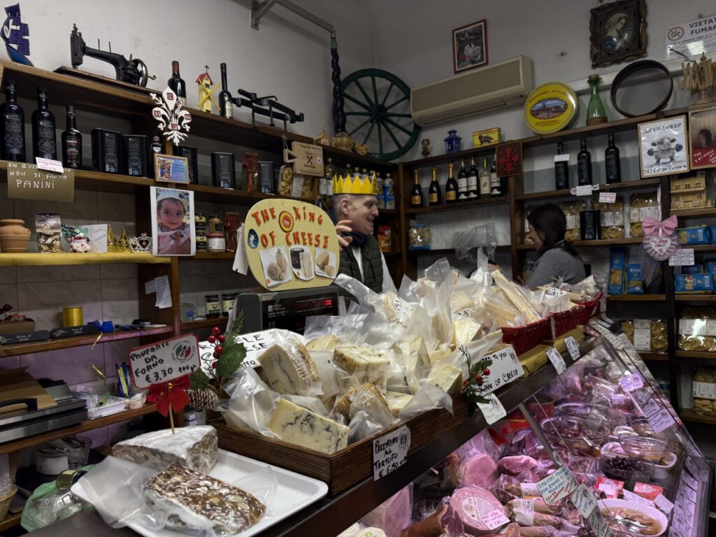A variety of cheese all over a counter with a man wearing a crown behind it.