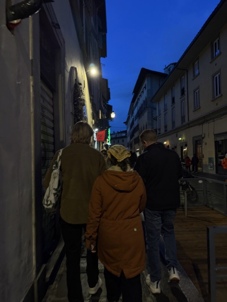 A group of people walk down the night streets of Florence.