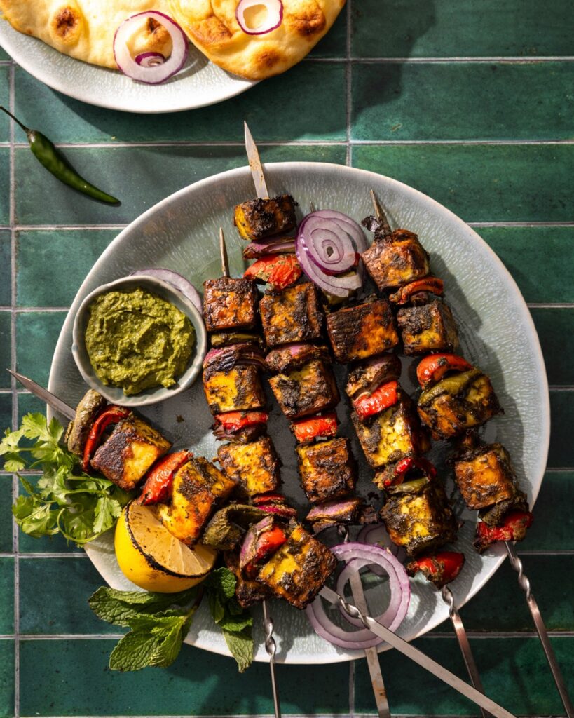 Skewers of Hariyali Paneer with vegetables on a plate with a green sauce beside it.