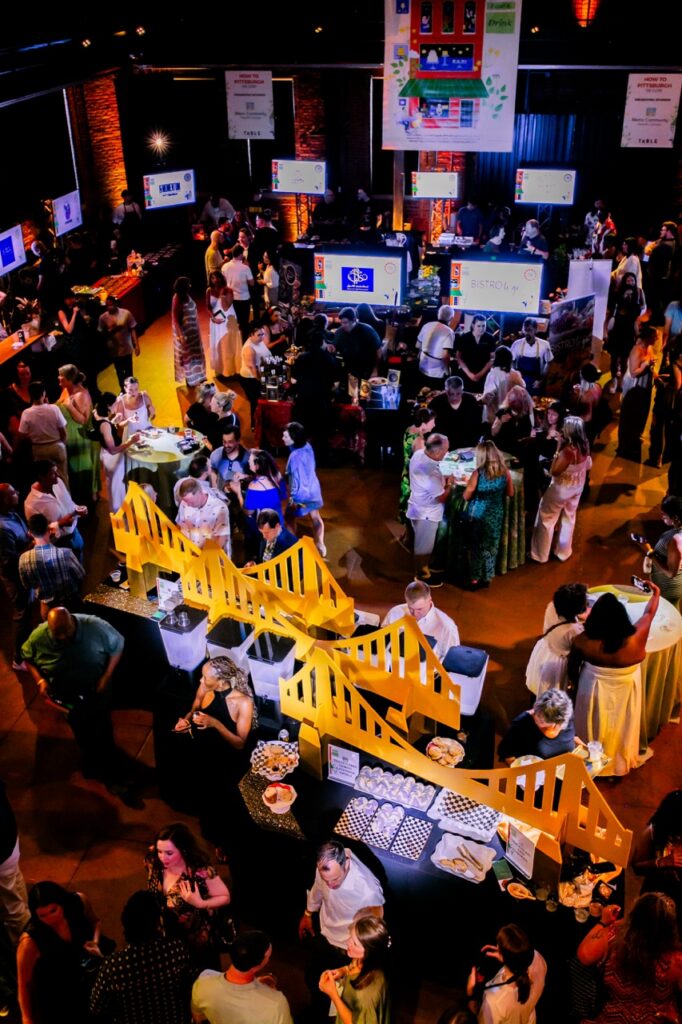 Groups of people gather around tables and yellow bridge decor at How to Pittsburgh.
