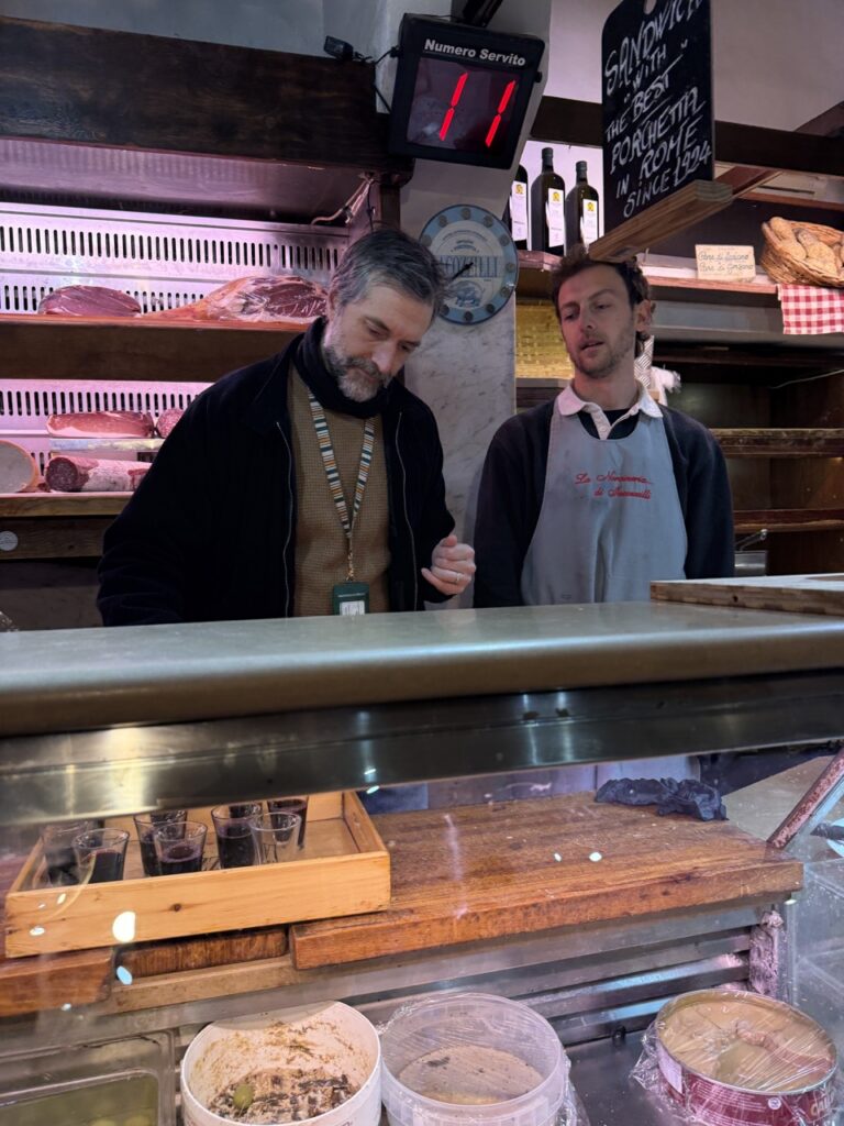 Two men stand behind a butcher counter in jakcets.