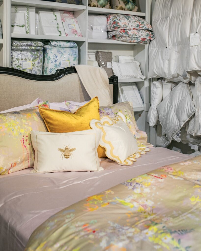 A demo bed with yellow and cream pillows featuring bee embroidery on it.