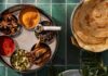 An Introduction to Indian Cuisine with Six Recipes A plate of Kerala-Style Dry Beef Stir-Fry on a green plate surrounded by herbs while a circular tray of spices sits adjacent to it.