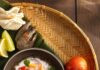 6 Authentic Filipino Recipes to Try at Home A small bowl of Kinilaw na Hipon (Filipino Ceviche) sits with a spoon in it on a woven tray next to tomatoes and citrus.