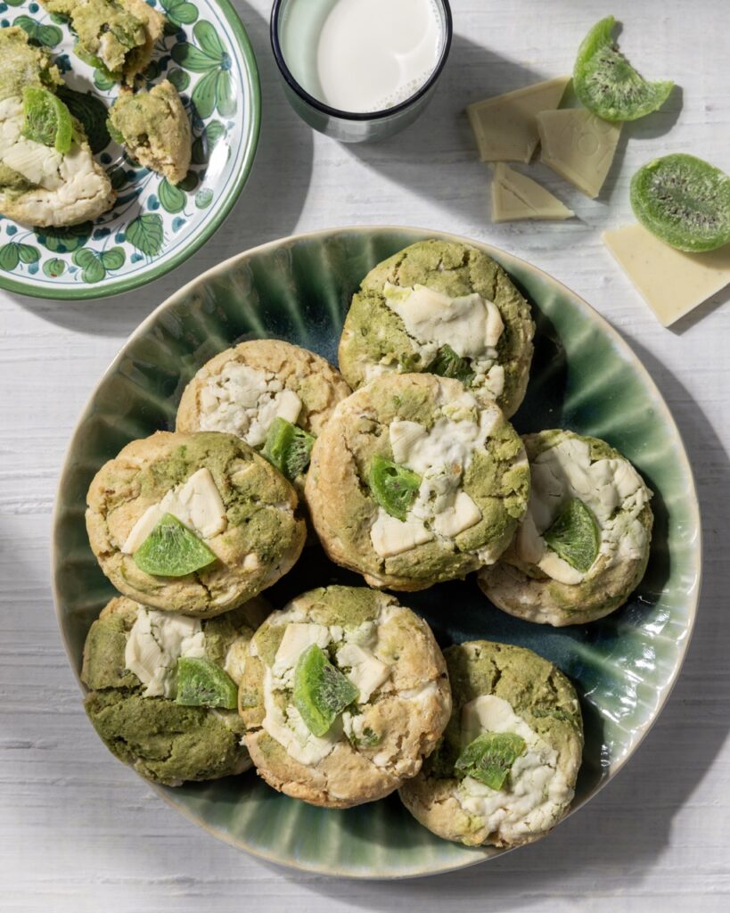 A green plate full of Kiwi Matcha White Chocolate Cookies with a cube of dried kiwi on top of each.