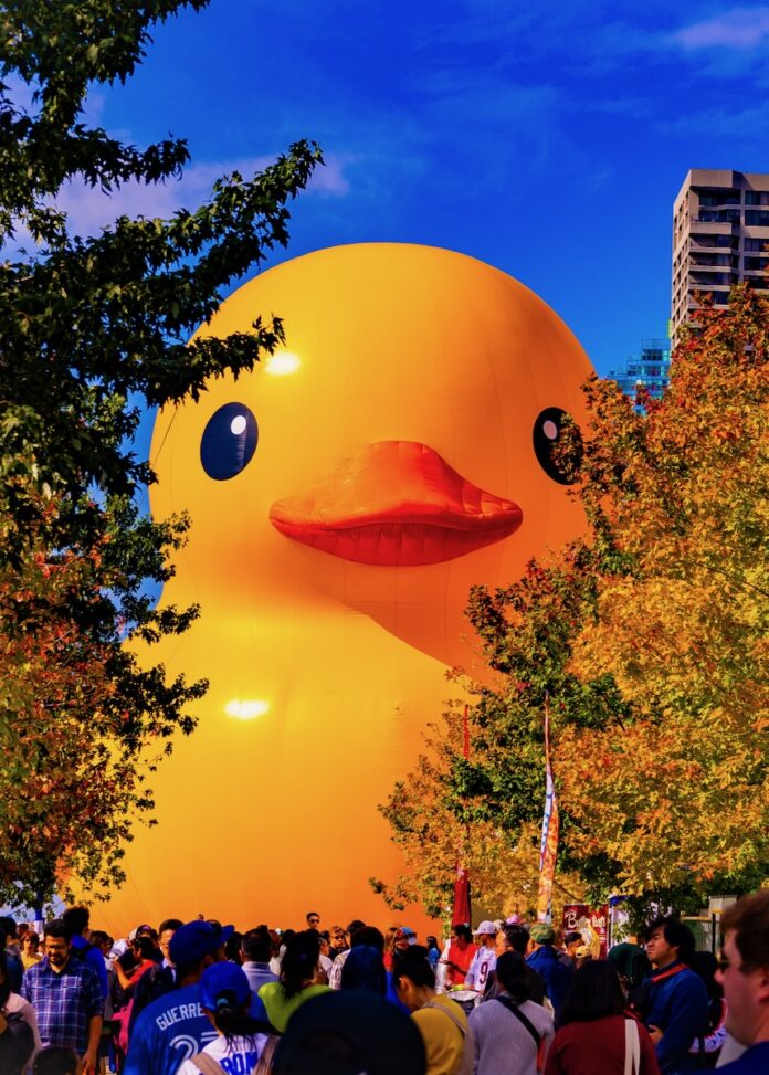 The world's largest rubber duck in a crowd slightly behind two trees.