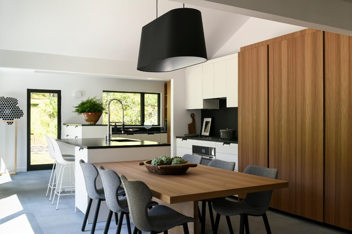 A minimalist Poliform kitchen in Fox Chapel featuring an elm wood dining table, sculptural grey B&B Italia chairs, a black architectural light fixture, and sleek white cabinetry.