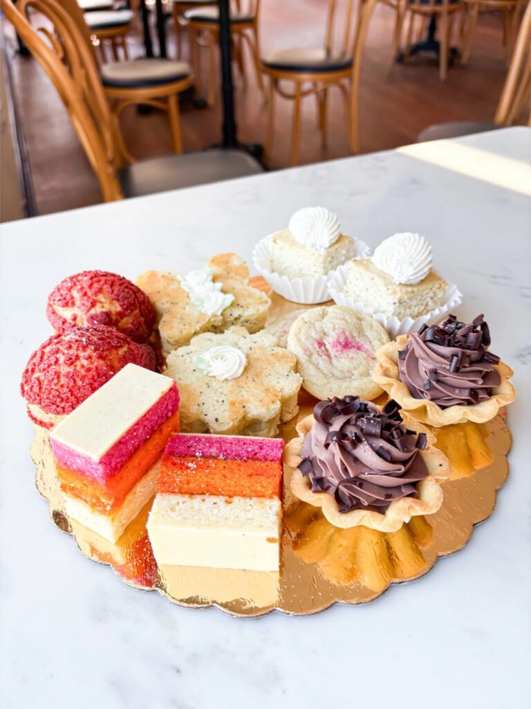 A gold plate of pastries with confections and other treats on a white marble table.