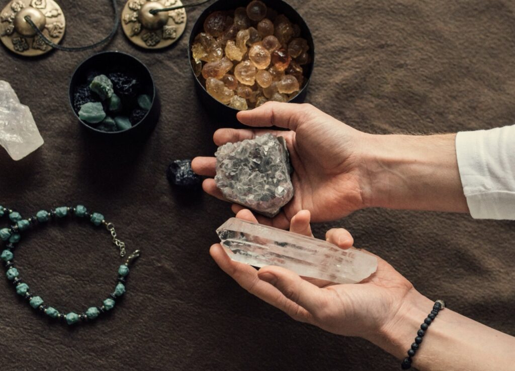 A person holds crystals over a table with more crystals and gems below in bowls. 