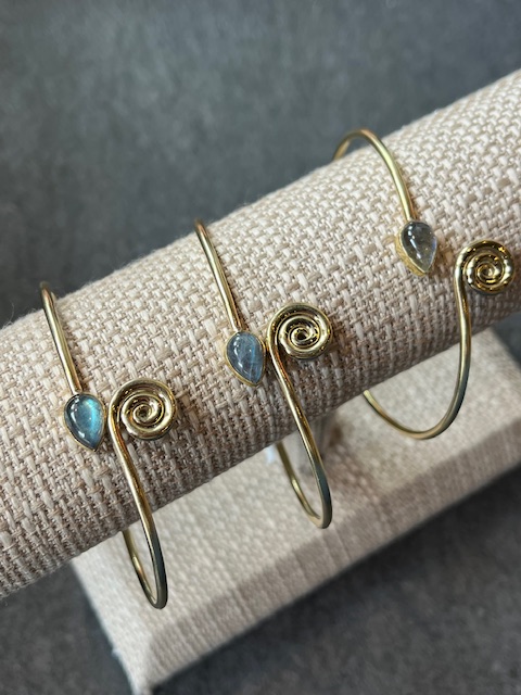 Three wrap around gold bracelets with a blue gem on a jewelry holder. 