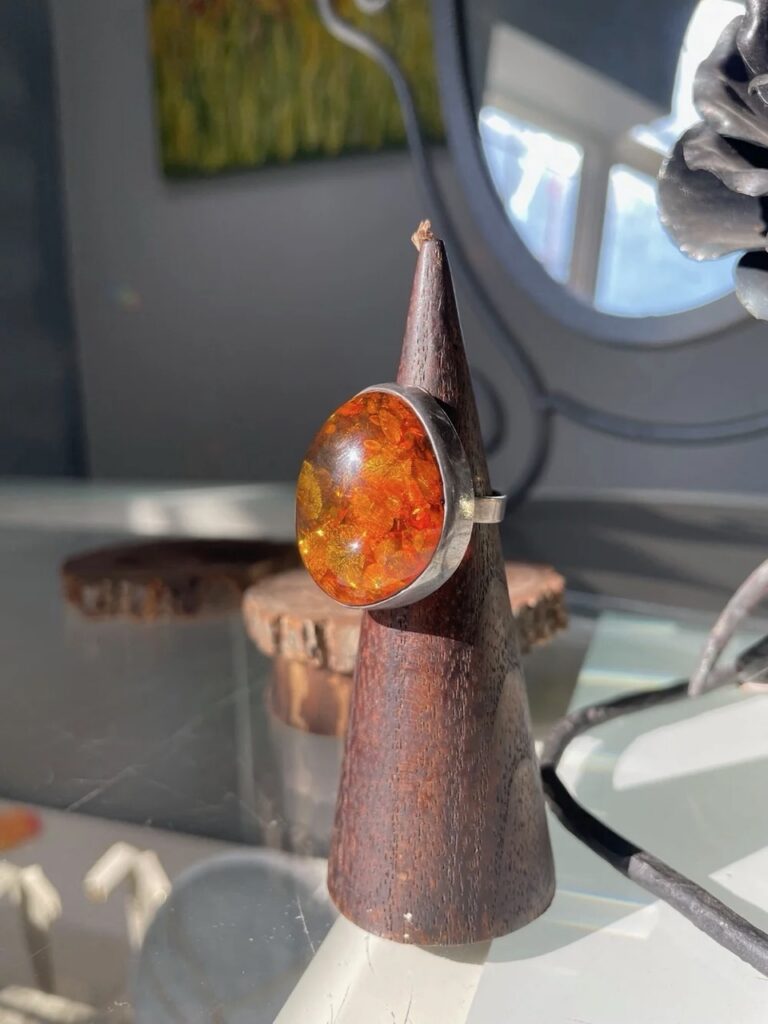 A silver ring with a large orange gem on the inside on a ring holder.