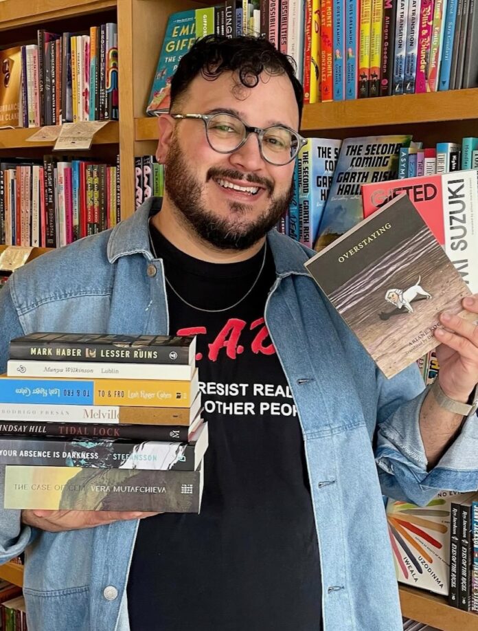 Pittsburgh's Best Literary Events for Bookworms May 2026 A bookkeeper at White Whale in Pittsburgh holds a stack of books in one hand and two other books in his other hand.