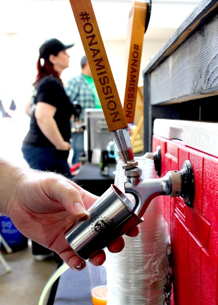 A man pours beer into a small metal cup for pour in the park.