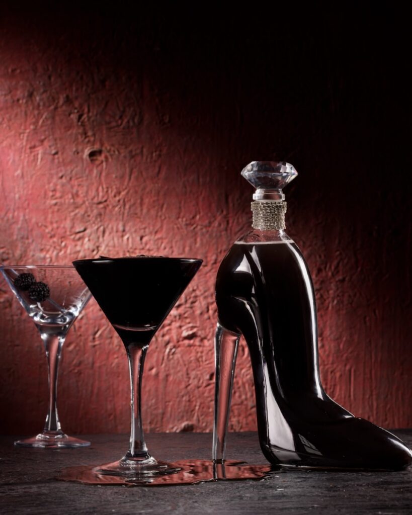 A dark filled martini glass sits beside a dark filled shoe glass container.