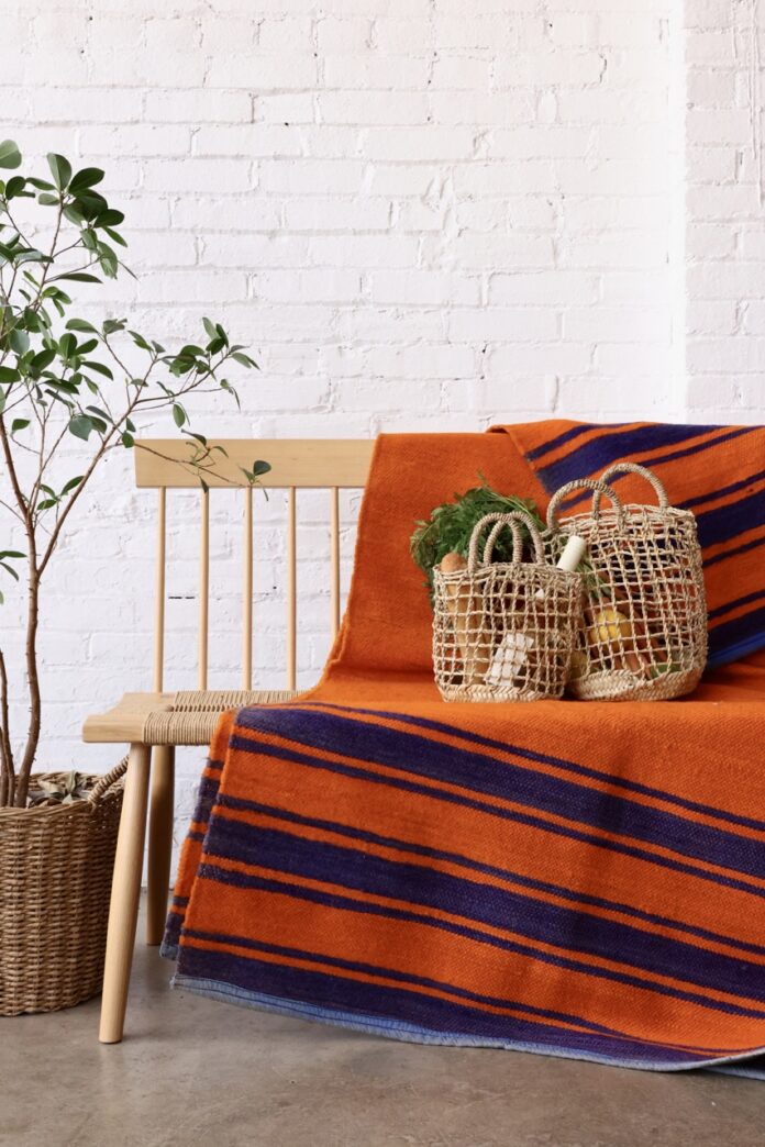 A wood bench with an orange and blue with netted bags on top of it.