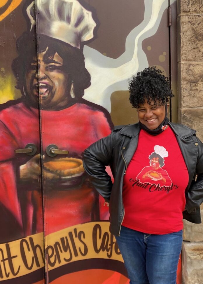 Pittsburgh Restaurants and the NFL Fight Student Hunger at Taste of the Draft Aunt Cheryl of Pittsburgh stands in a red shirt in front of a mural for her cafe that features her in a chefs hat.