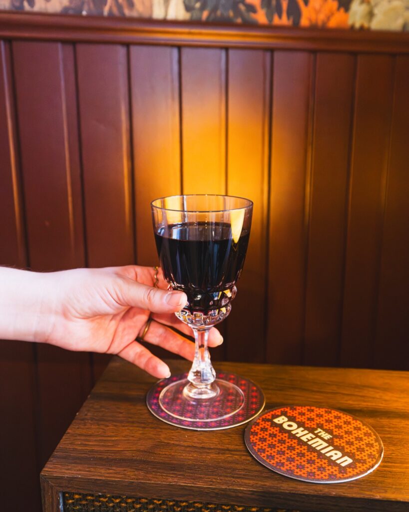 A wood booth where a person is setting down a glass of natural wine.