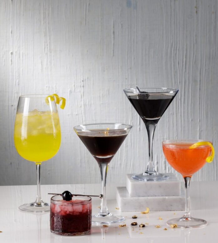 Five cocktails for The Devil Wears Prada 2 sit on a white table in tall and short glasses and various colors.