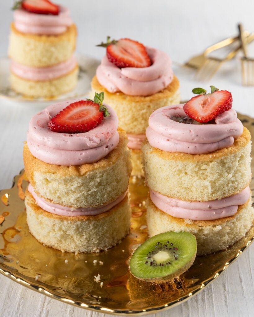 Three mini personal two-layer vanilla cakes with strawberry buttercream and kiwi jam in between the layers and a half strawberry on top.