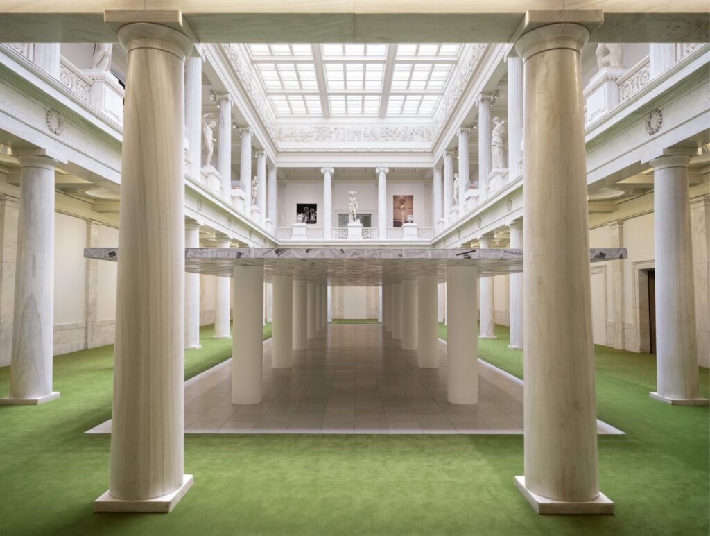 A green floor with white columns and a large marble slab in the middle of it.