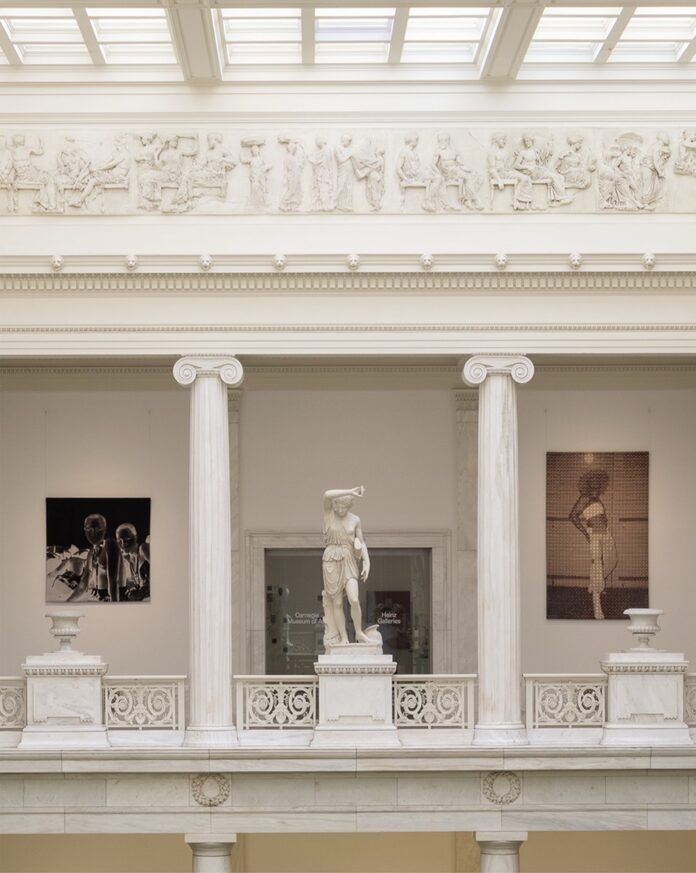 A white corridor with columns and marble statues behind a guard rail.