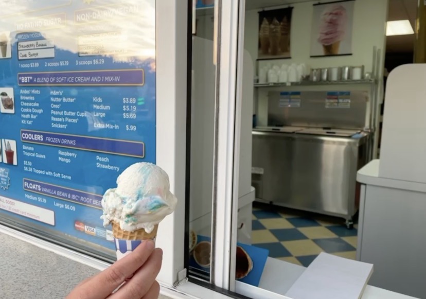 A birthday cake ice cream scoop on a cone by a parlor window.